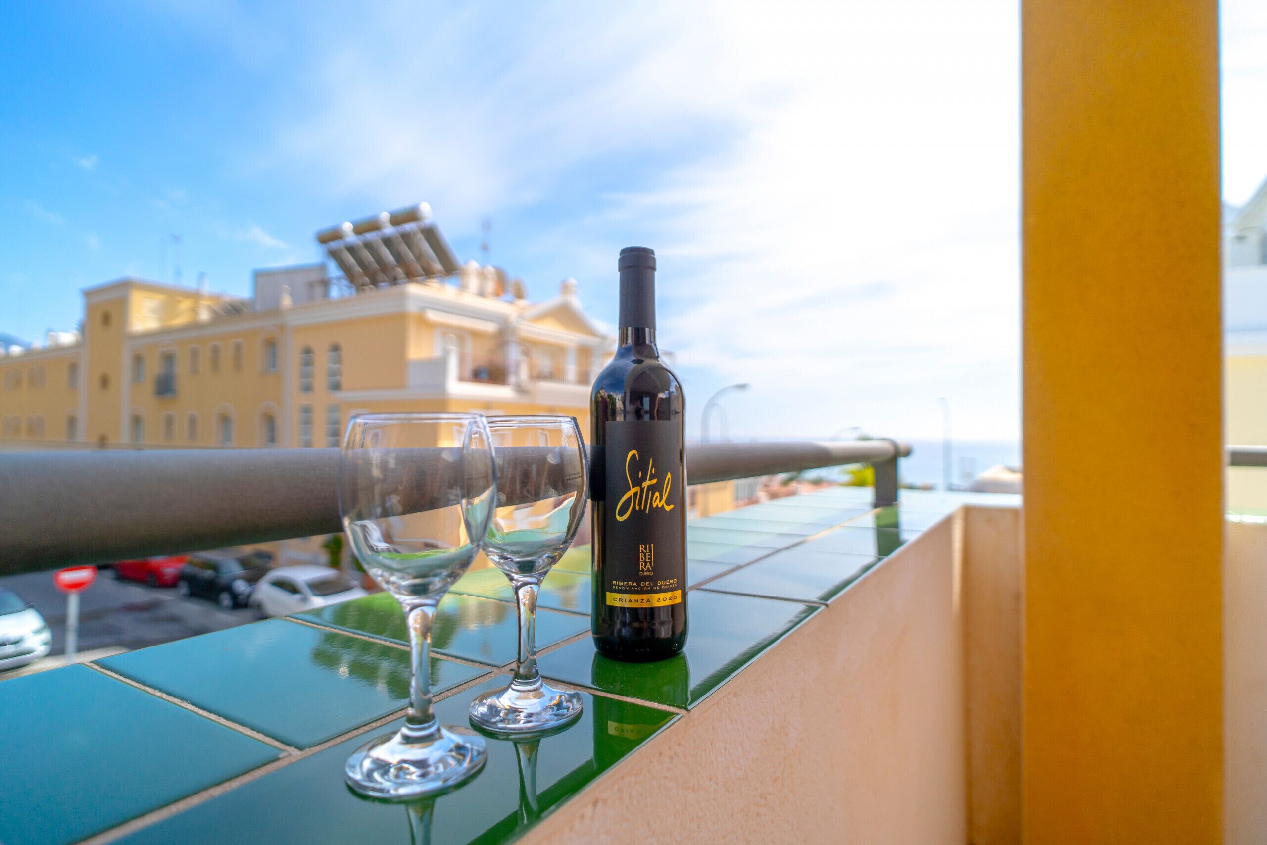 A bottle of Sittal wine and two glasses on a balcony with a city view.