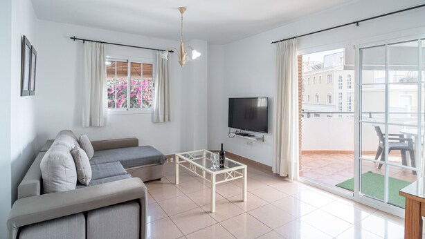 Una sala de estar moderna con un sofá, una mesa de centro de vidrio, un televisor de pantalla plana y una puerta corredera de vidrio que da a un área exterior.