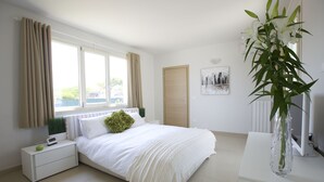 Un dormitorio moderno con cama, mesita de noche y un gran ventanal con cortinas.