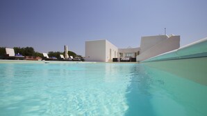 Una piscina con agua azul cristalina, sillas de descanso y un edificio moderno al fondo.