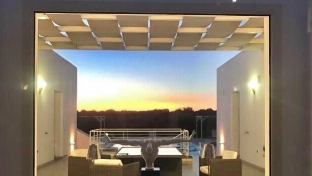 Un interior moderno con vistas al atardecer. Incluye una zona de estar con una mesa y sillas, además de una escultura decorativa.