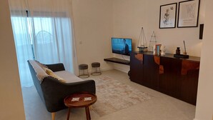 Ett modernt vardagsrum med en mörk soffa, en rund träpall, en tv och en liten bardisk med dekorativa föremål.