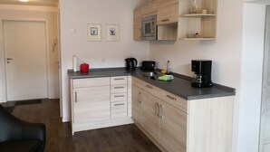 Cocina moderna con microondas, cafetera y un lavamanos pequeño. Se observan armarios de tonos claros y una encimera.
