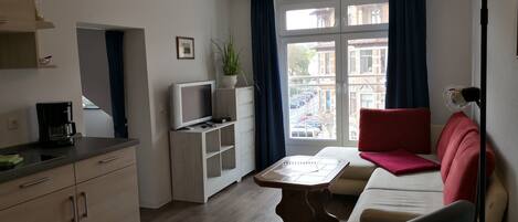 A modern living room with a sofa, a coffee table, a TV on a stand, and a dining table.