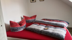 Una habitación pequeña con cama individual, colchón rojo y almohadas estampadas.