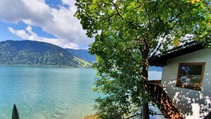 Eine Blockhütte am Seeufer mit einer Holzdiele und Blick auf See und Berge.