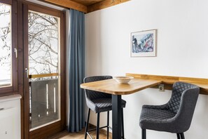 A dining area with a wooden table and two chairs, a window with a view of bare trees, and a framed picture on the wall. - Waterfront Apartment 4 (Zell am See)