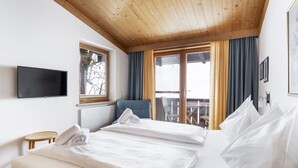 Ein Hotelzimmer mit zwei Betten, einem Fernseher, einem Fenster und einem Balkon mit Vorhängen.