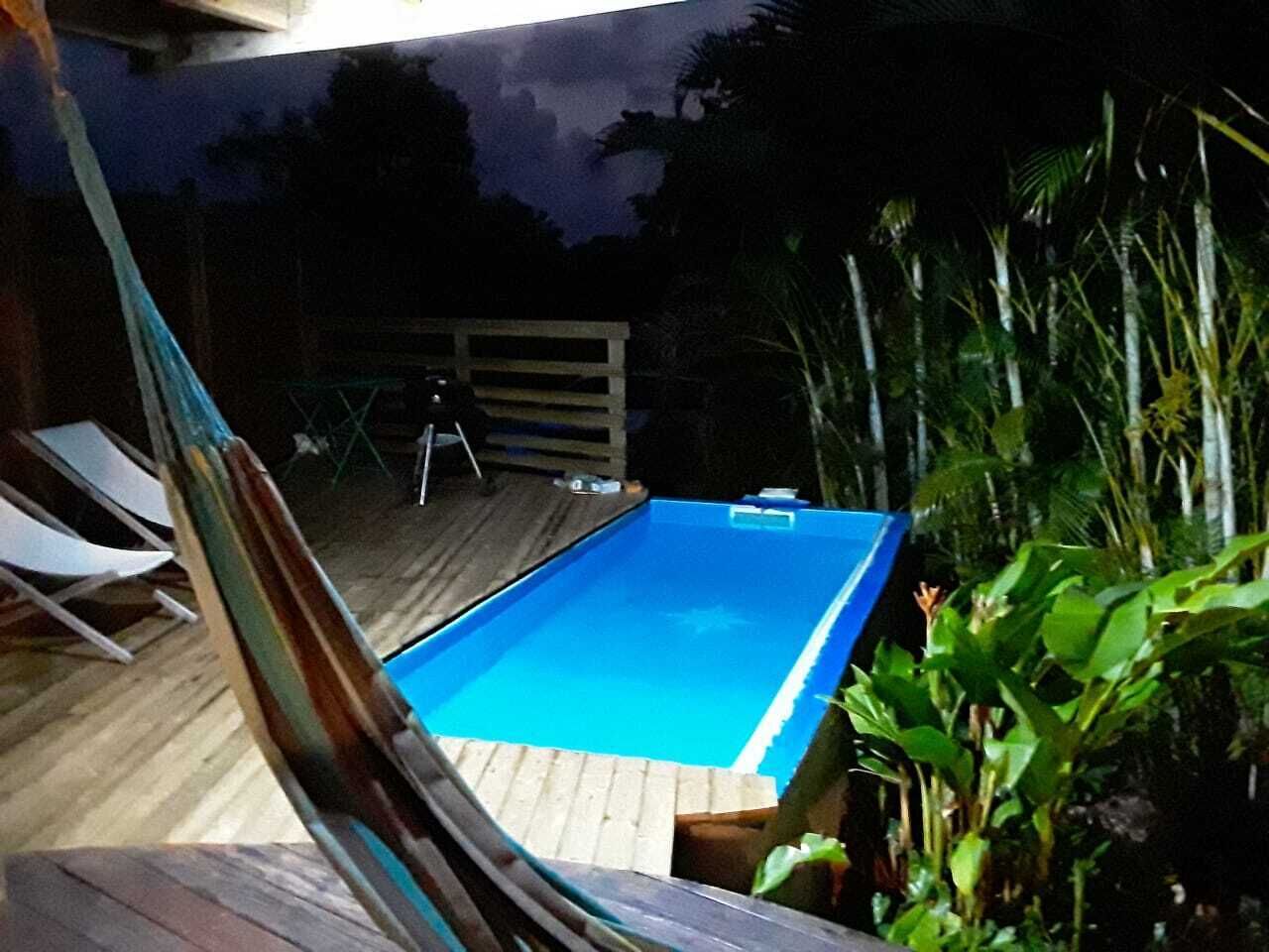 Une piscine rectangulaire dotée d’une terrasse en bois, entourée d’une végétation luxuriante.