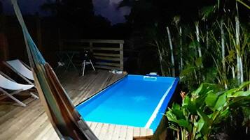 Une piscine rectangulaire dotée d’une terrasse en bois, entourée d’une végétation luxuriante.