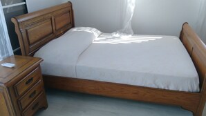 Ein hölzernes Bett mit Baldachin, ein Nachttisch mit Schubladen und eine schlichte Wand.
