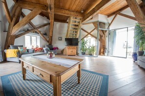 A spacious loft with exposed wooden beams, a wooden dining table, and a cozy seating area with a sofa and armchairs. - Enjoy your holidays in the historic, romantic windmill Catharina (Oldenswort)