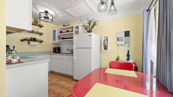 A compact kitchen with white cabinets, a red dining table, and a refrigerator.
