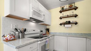 A kitchen with white cabinets, a microwave, a stove, and a countertop. There are shelves on the wall above the countertop. - The Hideaways at Point Pleasant (Pine Side) (Bradenton)