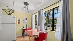 A compact kitchen with a white refrigerator, a dining table with red chairs, and a window with curtains. - The Hideaways at Point Pleasant (Pine Side) (Bradenton)