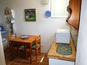 Een kleine keuken met een houten tafel, stoelen, een magnetron en een klein plankje met keukengerei.