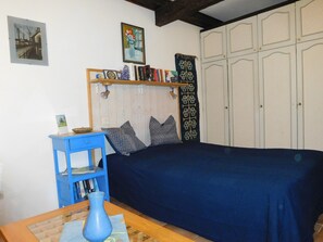 Een slaapkamer met een bed, een blauwe tafel met een vaas, een boekenplank en een garderobe.