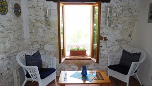 Une pièce comprenant deux fauteuils en osier avec des coussins noirs, une table en bois sur laquelle est posé un vase bleu, et une fenêtre donnant sur un paysage verdoyant.