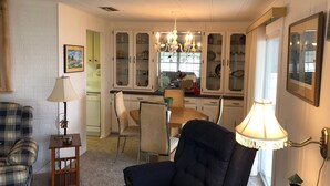 A living room with a dark blue armchair, a small wooden side table, a lamp, and a dining area with a wooden table and chairs.