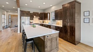 Una cocina moderna con armarios de madera oscura, una isla grande con taburetes e iluminación empotrada en el techo.