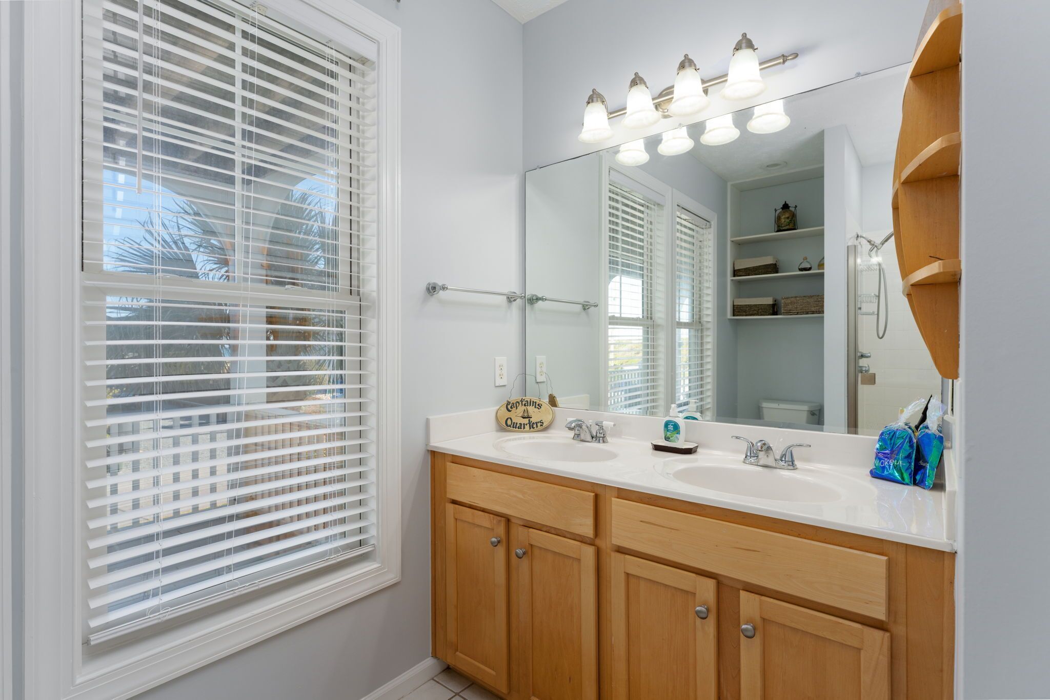 Une salle de bain avec un grand miroir, un meuble-lavabo blanc et une fenêtre équipée de stores.