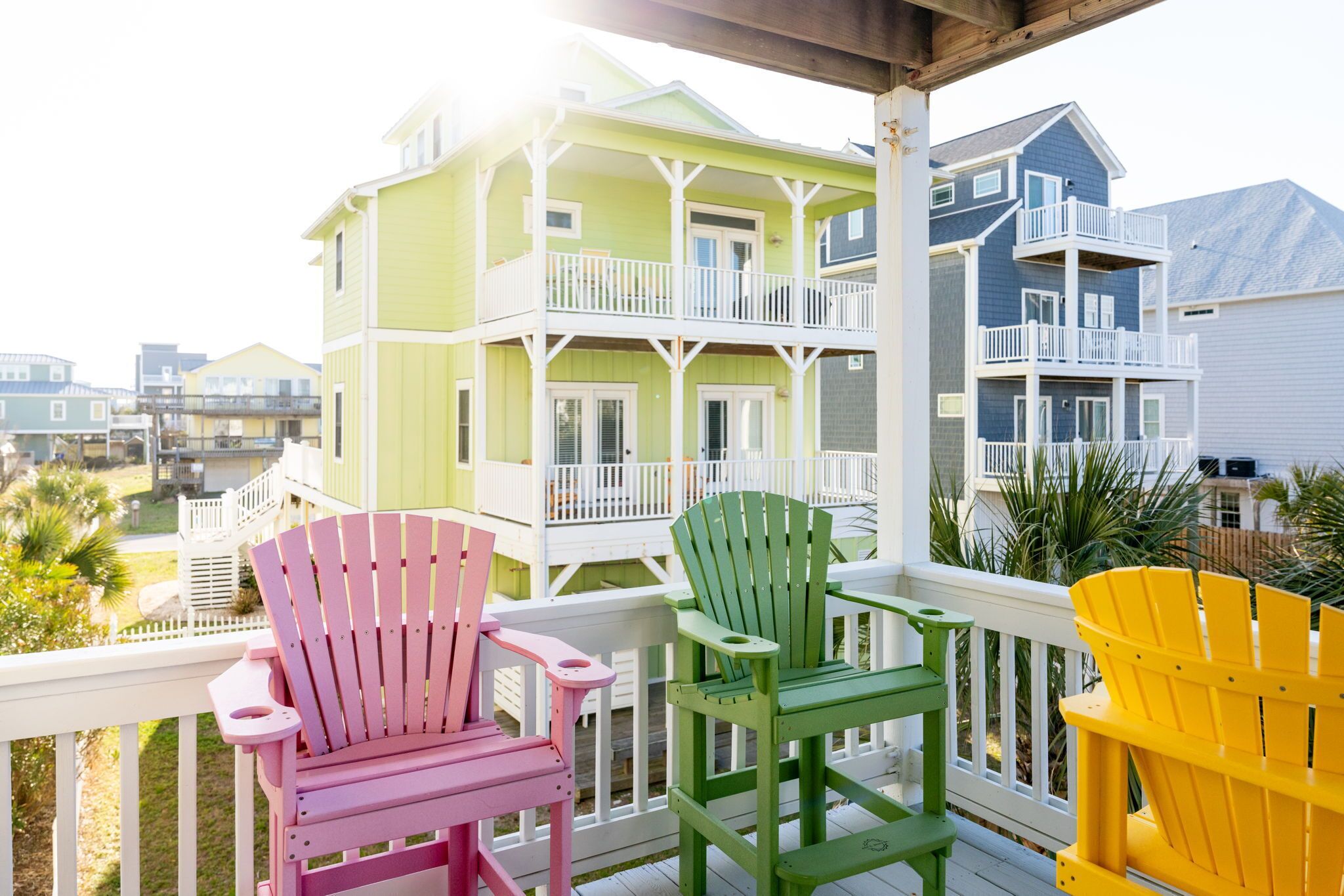 Un balcon agrémenté de chaises Adirondack aux couleurs vives, un immeuble à plusieurs étages doté de balcons, et une vue sur d’autres bâtiments.