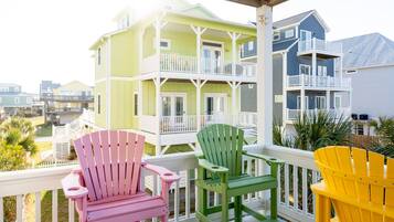 Un balcon agrémenté de chaises Adirondack aux couleurs vives, un immeuble à plusieurs étages doté de balcons, et une vue sur d’autres bâtiments.