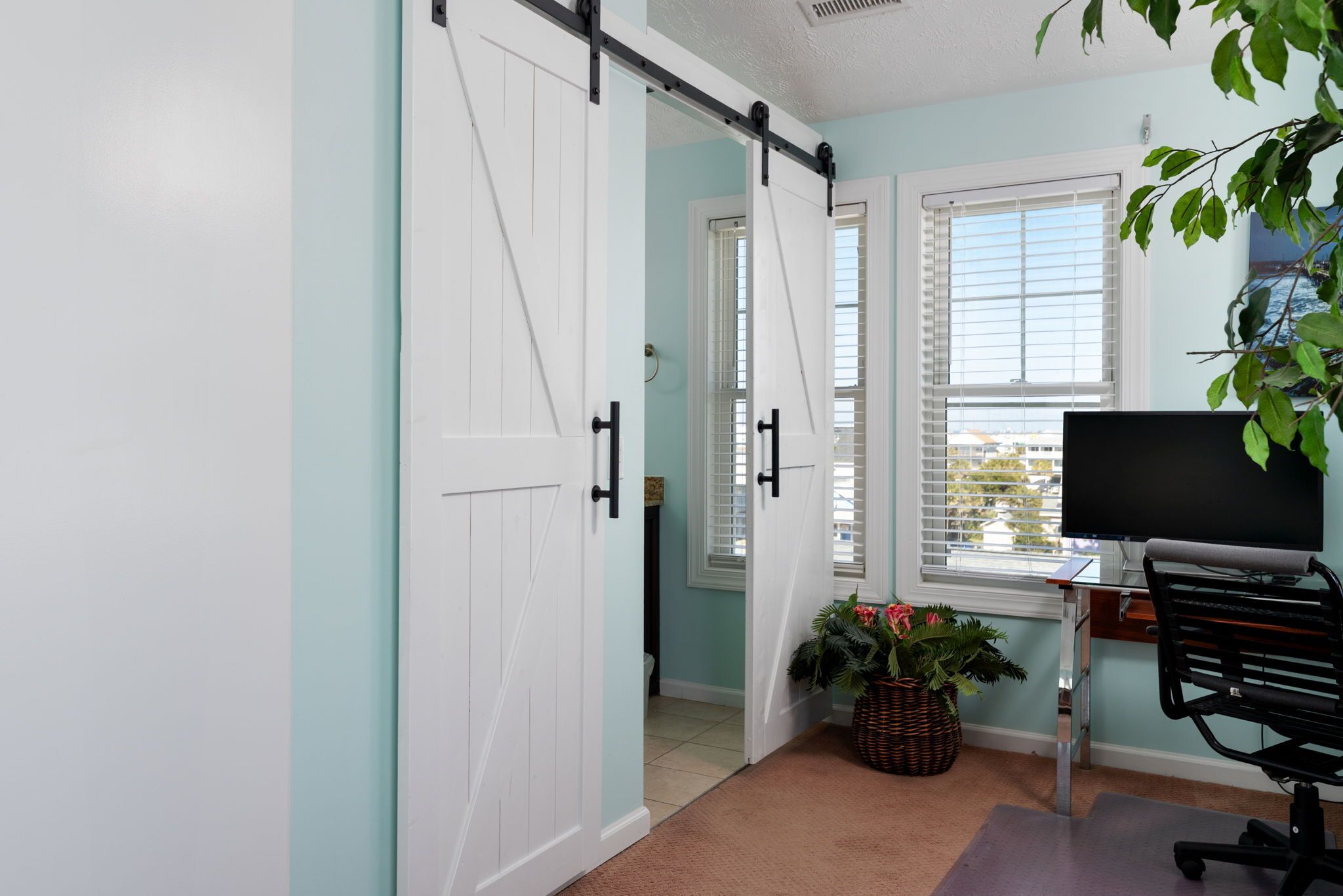A room with a sliding door, a desk with a computer, a chair, and a potted plant.