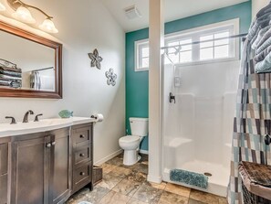 Un baño con un lavamanos blanco, muebles oscuros, un inodoro blanco y una zona de ducha.
