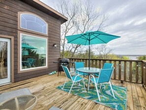 A wooden deck with a table and chairs, a grill, and a view of the landscape.