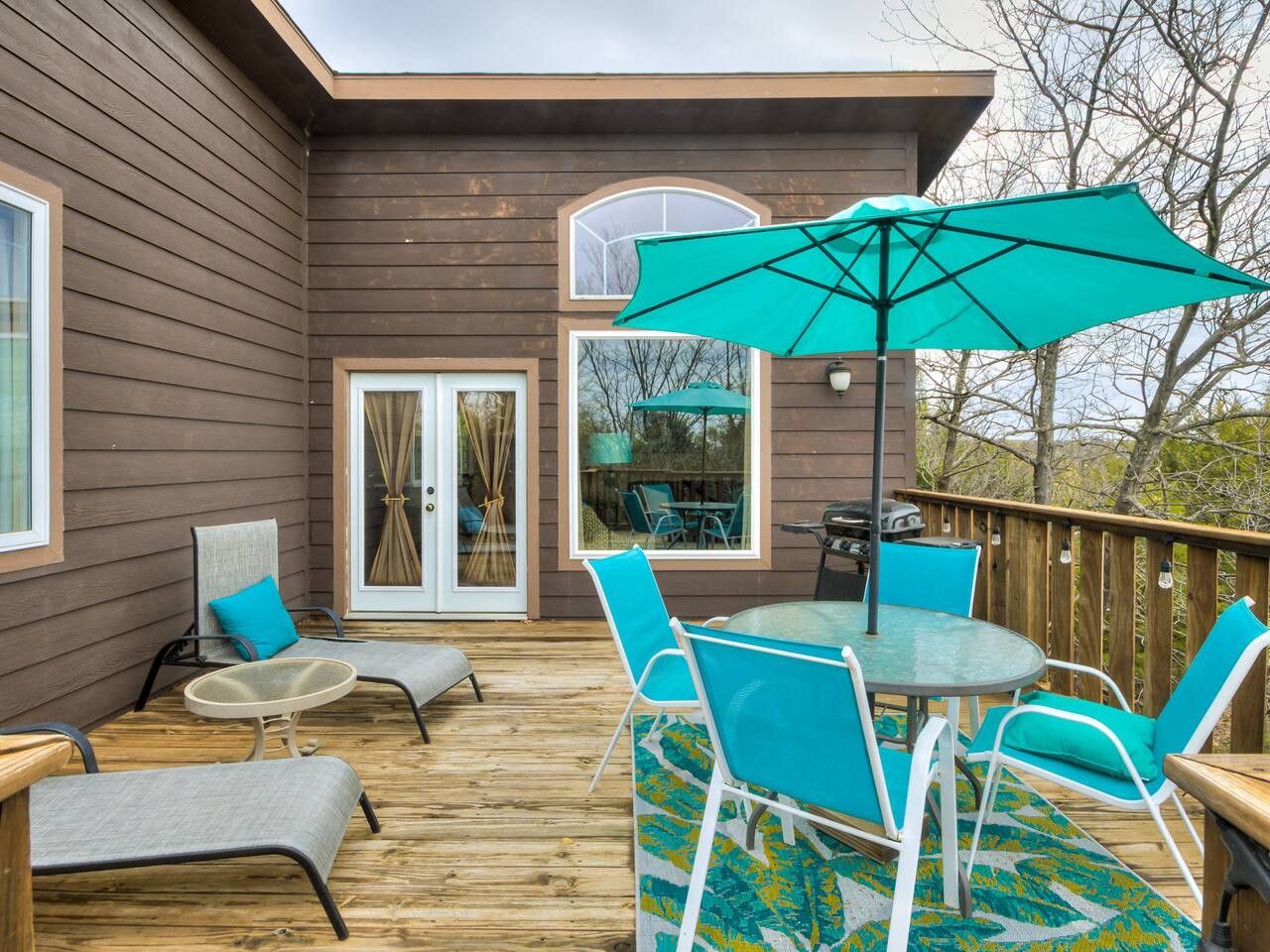 Eine Holzterrasse mit Gartenmöbeln, darunter ein Tisch und Stühle, sowie ein großer Sonnenschirm.