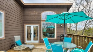 Une terrasse en bois aménagée avec du mobilier d’extérieur, notamment une table et des chaises, ainsi qu’un grand parasol.
