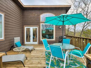 Una terraza de madera con mobiliario exterior, incluyendo una mesa y sillas, y un paraguas grande.