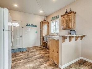 Una cocina con piso de madera en patrón de espiga, gabinetes de madera, microondas integrado y una pequeña isla con pileta.