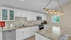 A modern kitchen with white cabinets, a granite countertop, a built-in microwave, a gas stove, and a hanging light fixture. - Ground Floor Luxury 4BR Home · Heated Saltwater Pool & Spa · Very Close to Beach (Holmes Beach)