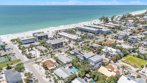 An aerial view of a coastal residential area with beachfront properties, including houses with swimming pools and a beach in the background. - Ground Floor Luxury 4BR Home · Heated Saltwater Pool & Spa · Very Close to Beach (Holmes Beach)
