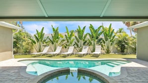 A swimming pool with a curved edge, surrounded by a paved area and a row of white lounge chairs. - Ground Floor Luxury 4BR Home · Heated Saltwater Pool & Spa · Very Close to Beach (Holmes Beach)