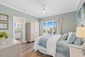 A bedroom with a bed, a dresser, a nightstand, a ceiling fan, and a window with curtains.
