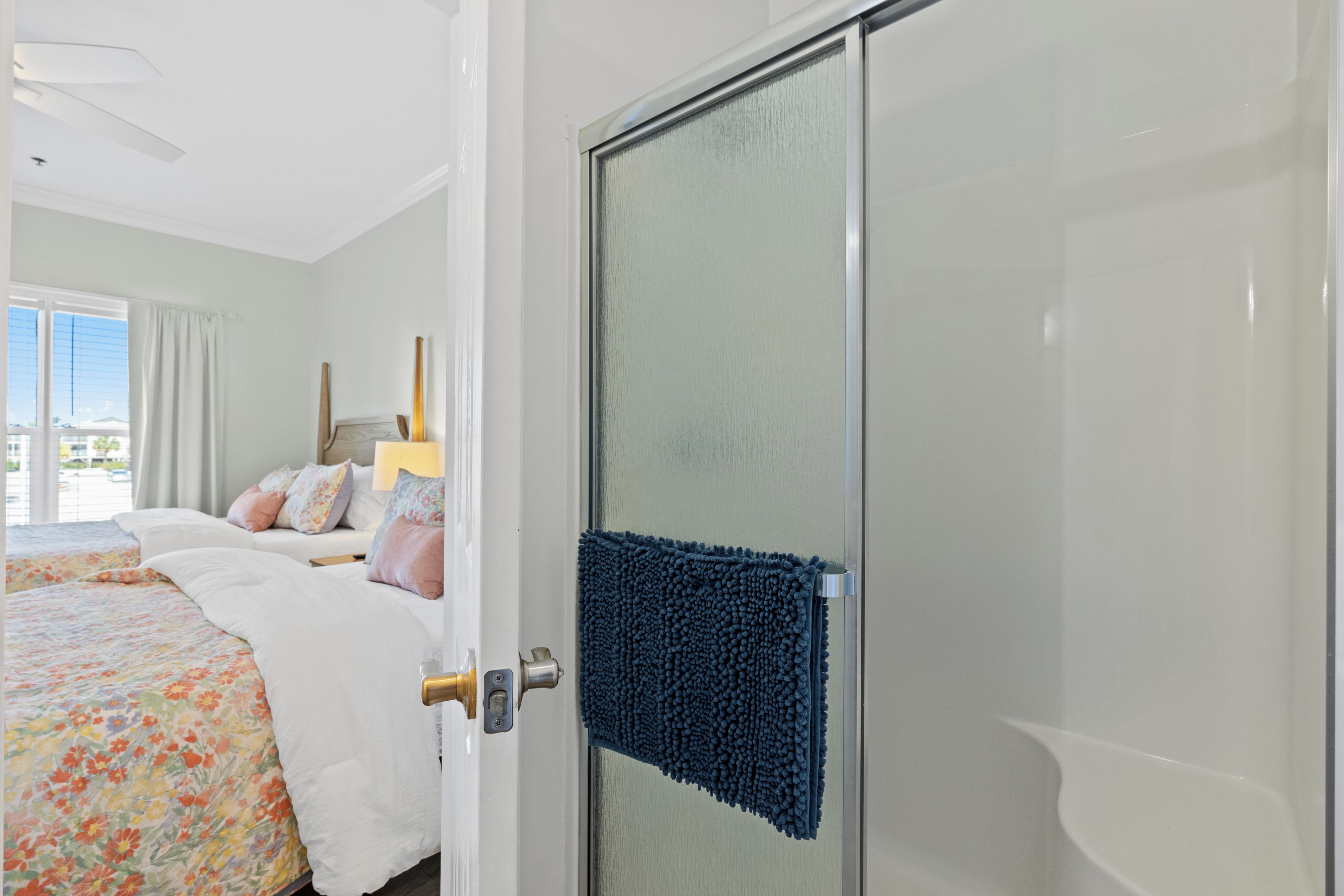 A bedroom with a bed, a bathroom with a glass door, and a view of the outdoors.