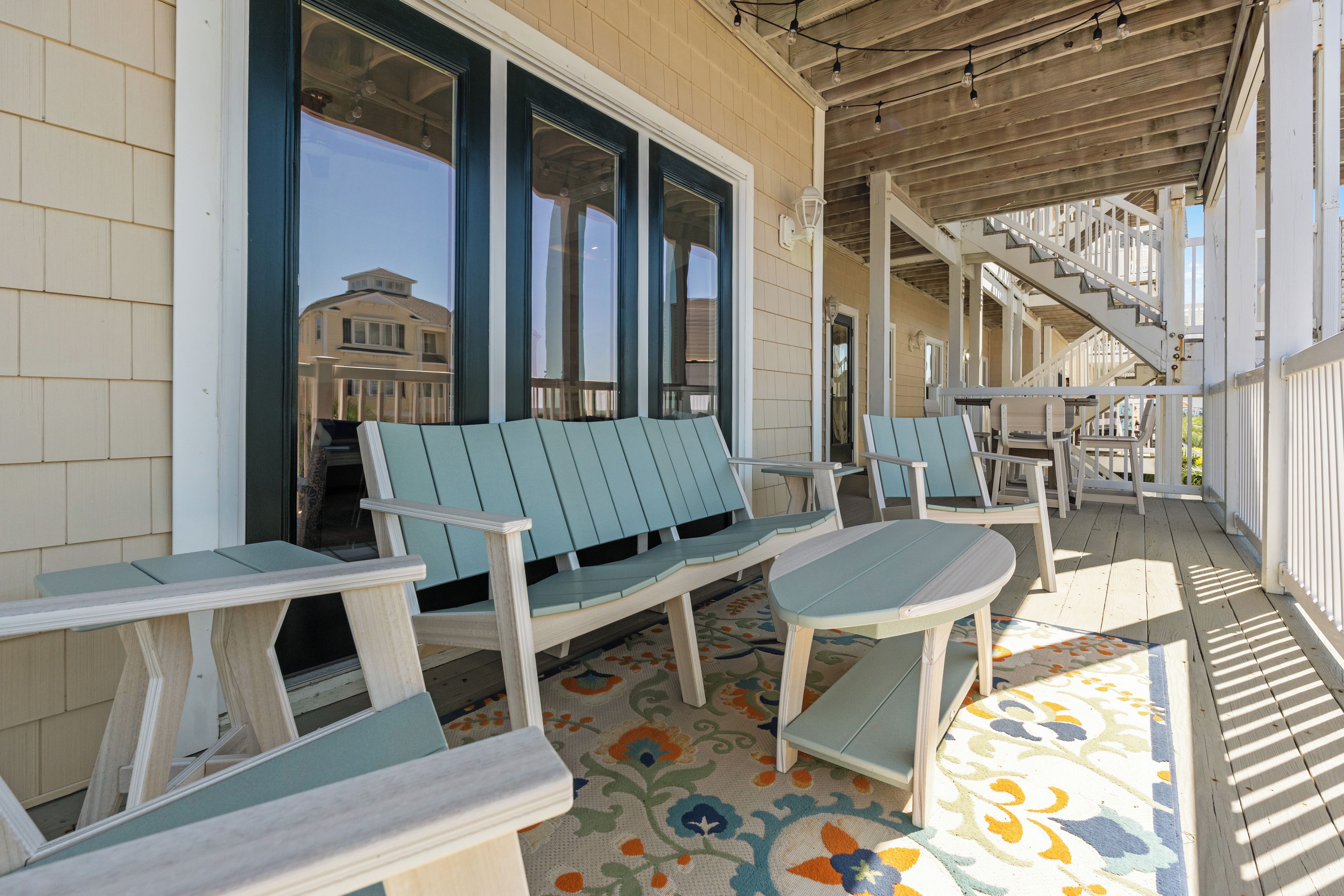 A covered porch with outdoor seating, a staircase, and a view of a building in the background.