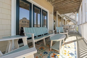 A covered porch with outdoor seating, a staircase, and a view of a building in the background. - Castaway the Day - Second Row -closest walk to beach access, pool, and tiki bar! (Ocean Isle Beach)