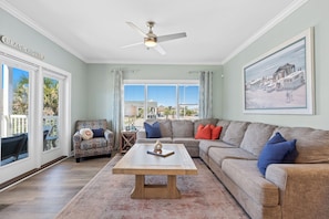 A living room with a sofa, armchair, coffee table, ceiling fan, and a painting on the wall.