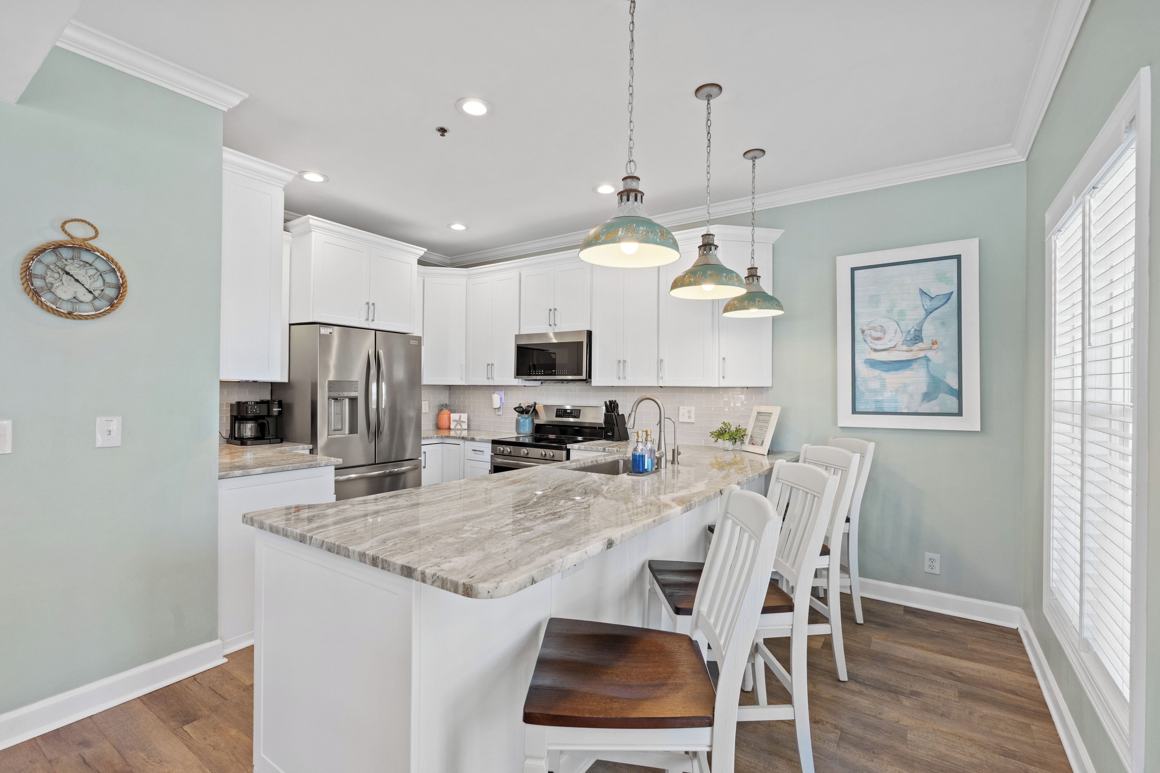 A modern kitchen with white cabinets, a marble island, and pendant lighting.