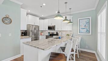 A modern kitchen with white cabinets, a marble island, and pendant lighting.