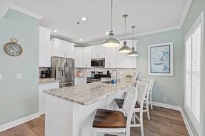 A modern kitchen with white cabinets, a marble island, and pendant lighting.