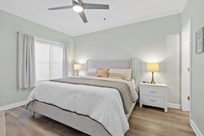 A bedroom with a bed, two bedside tables, a ceiling fan, and a window with curtains.