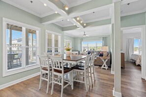 A spacious living area with a dining table, white chairs, a sofa, and a ceiling fan.