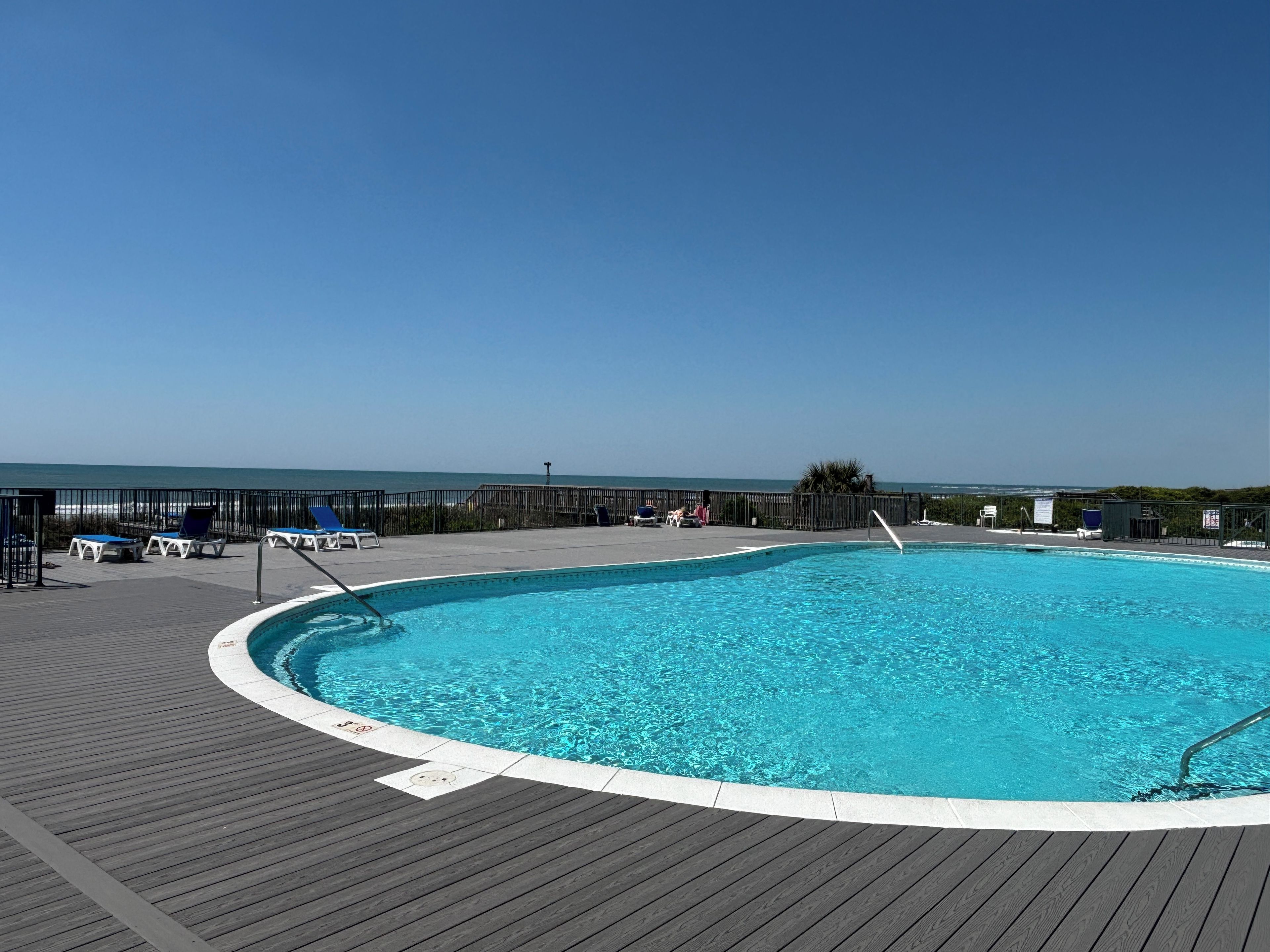A swimming pool with a wooden deck, lounge chairs, and a view of the ocean.