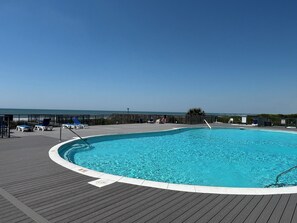 A swimming pool with a wooden deck, lounge chairs, and a view of the ocean.