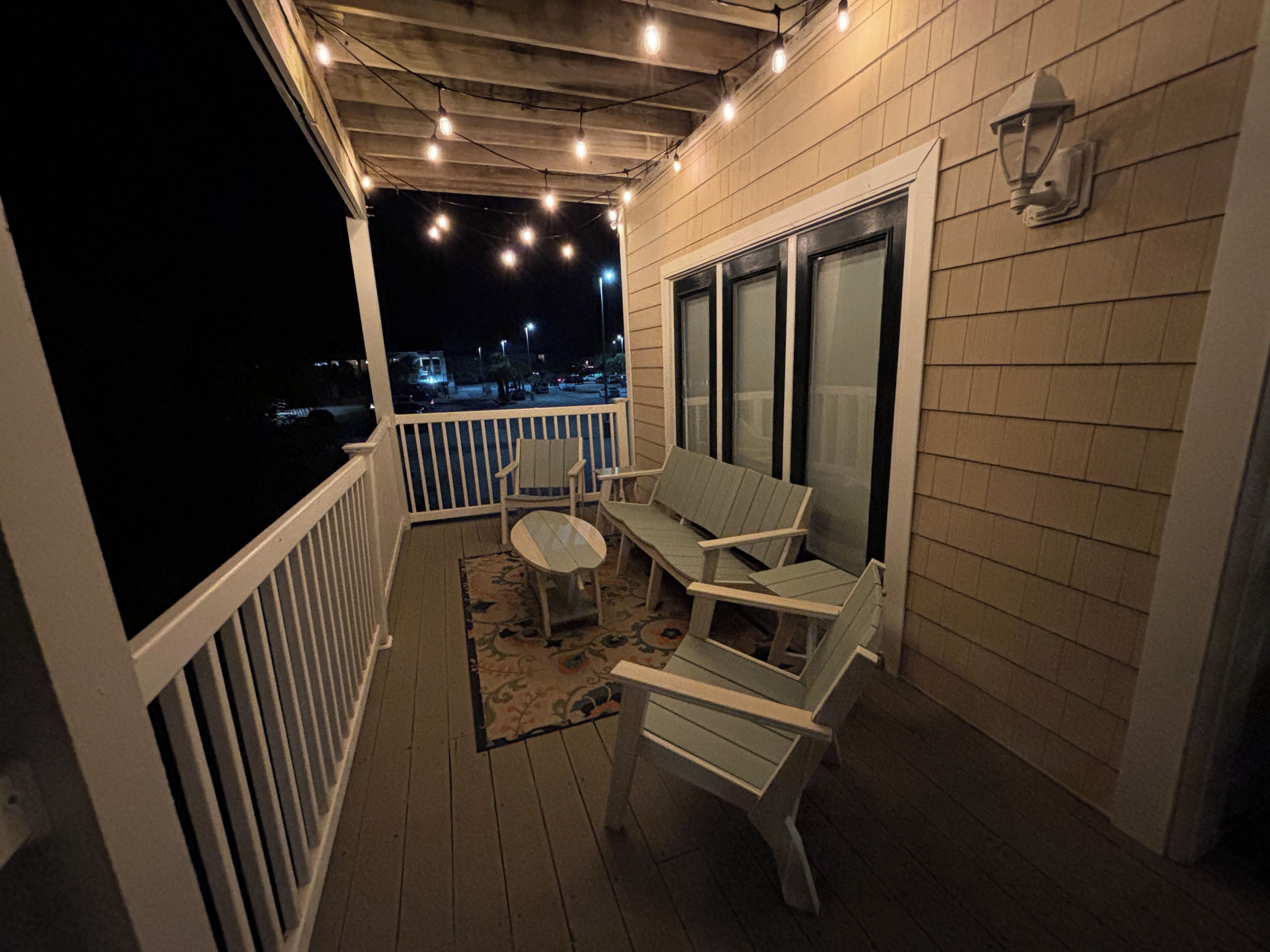 Un espace extérieur abrité, doté d’une terrasse en bois, de mobilier d’extérieur blanc et de guirlandes lumineuses.